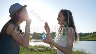 有趣的青少年，带着肥皂泡的快乐姐妹在背光的草坪上快乐地度过闲暇时光